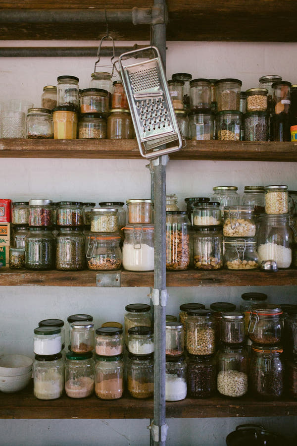 Glass jars of pantry staples and ingredients on wooden shelves