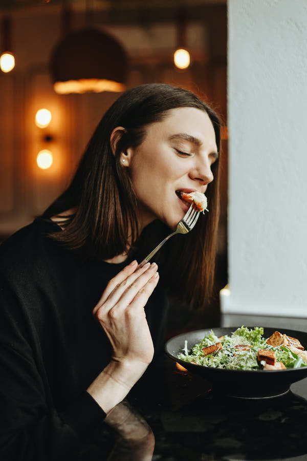 A woman tasting a small forkful of food with her eyes closed, savouring the flavour