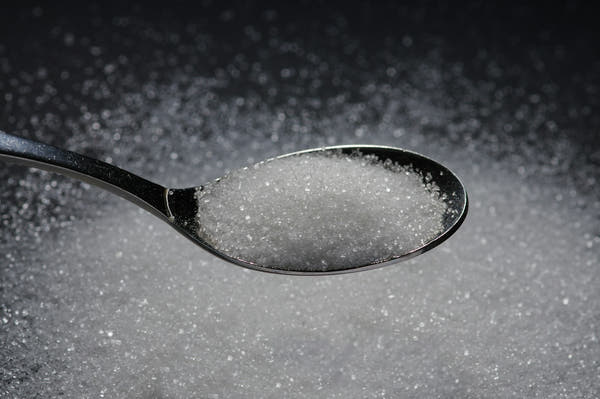 A spoon of fine white monk fruit sweetener over a dark surface