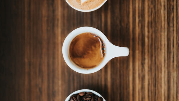 A person tasting from a small spoon by a mug of coffee in warm natural light