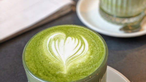 Matcha latte in a glass beside a bamboo whisk in bright natural light
