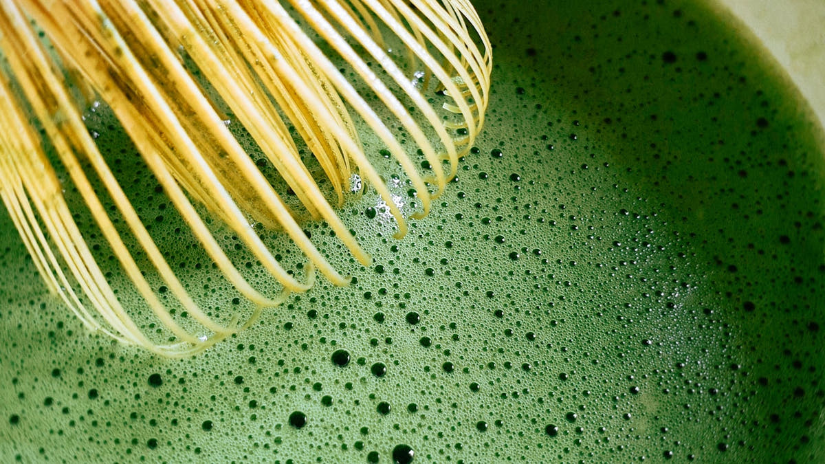 A whisked bowl of bright green matcha with a bamboo whisk in bright natural light