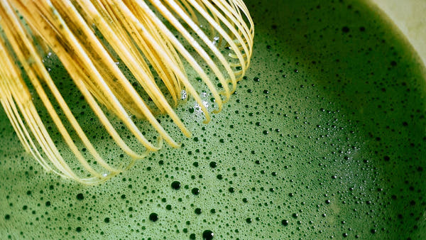 A whisked bowl of bright green matcha with a bamboo whisk in bright natural light