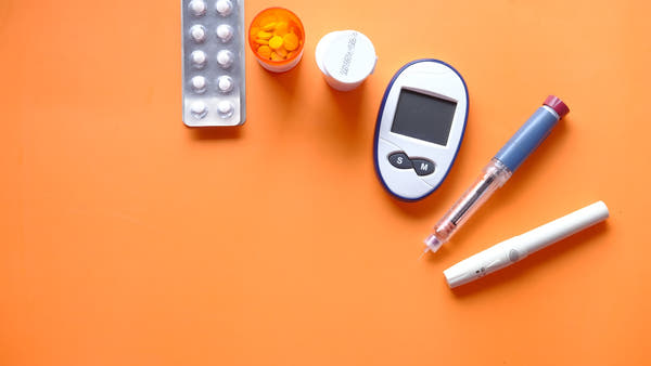 A blood glucose meter on a light surface alongside health items