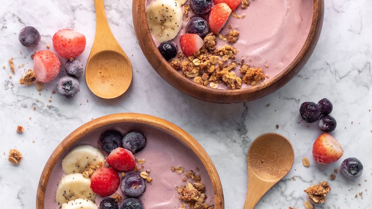 Bowl of Greek yoghurt topped with fresh berries and a spoon in bright natural light