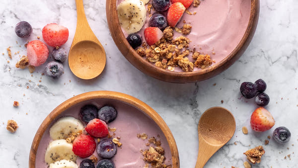 Bowl of Greek yoghurt topped with fresh berries and a spoon in bright natural light