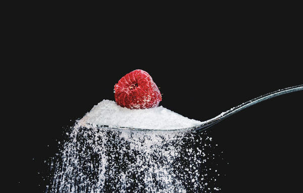 A raspberry resting on a spoonful of pure white sweetener
