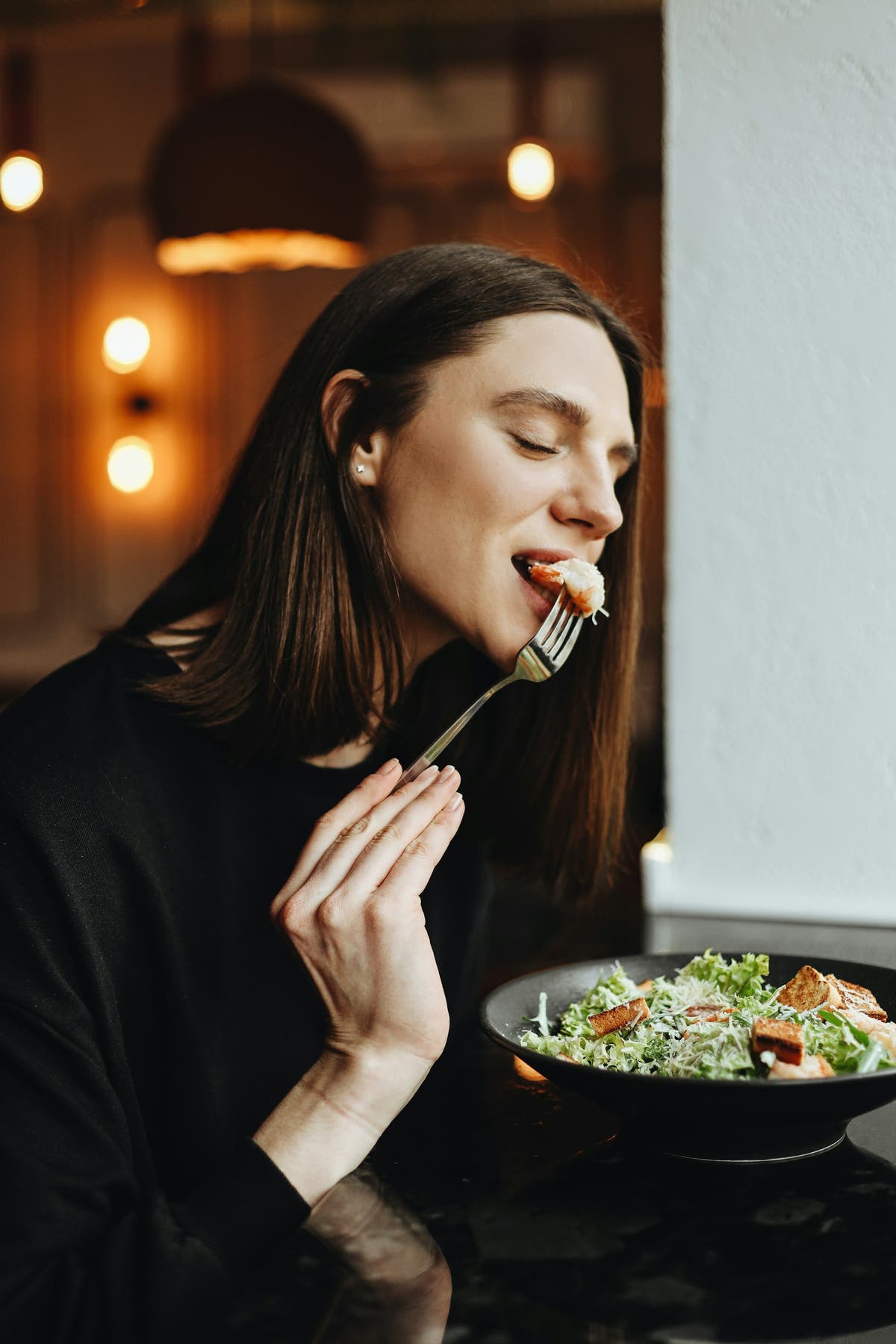 A woman tasting a small forkful of food with her eyes closed, savouring the flavour