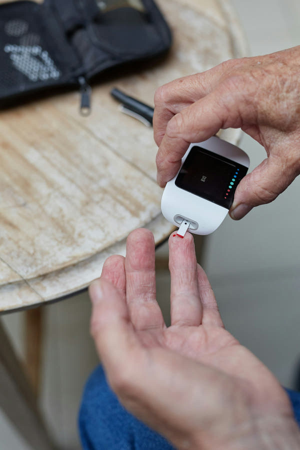 A finger-prick blood glucose meter being used on a hand